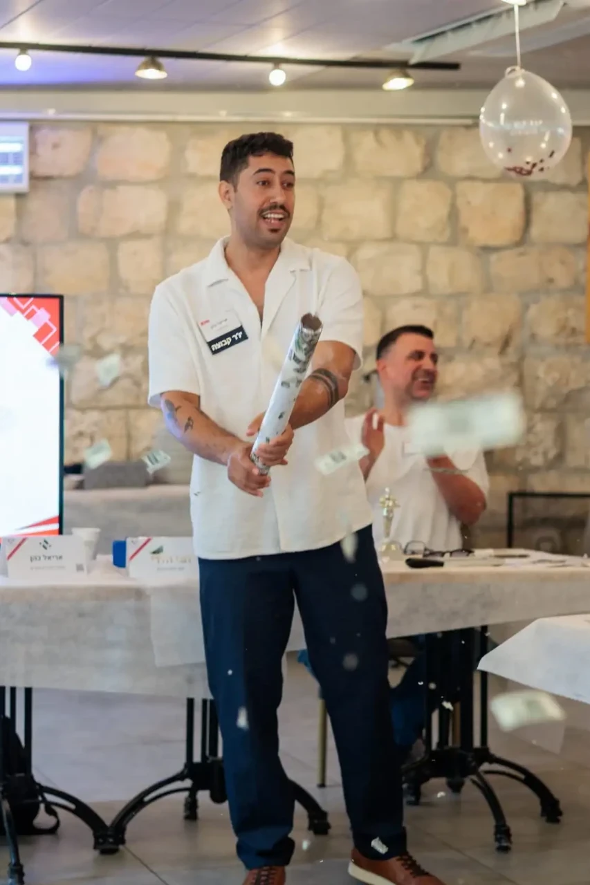 חבר קבוצת הבירה משיק תותח קונפטי במפגש מול מסך ההודעות, חבריו מוחאים כפיים